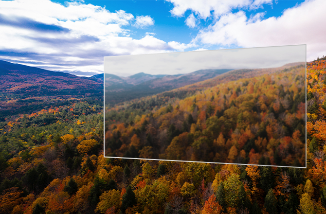 The image shows a transparent display floating above a mountainous landscape with a colorful autumn forest and blue sky, but the display is blurry due to the lack of tandem OLED technology.