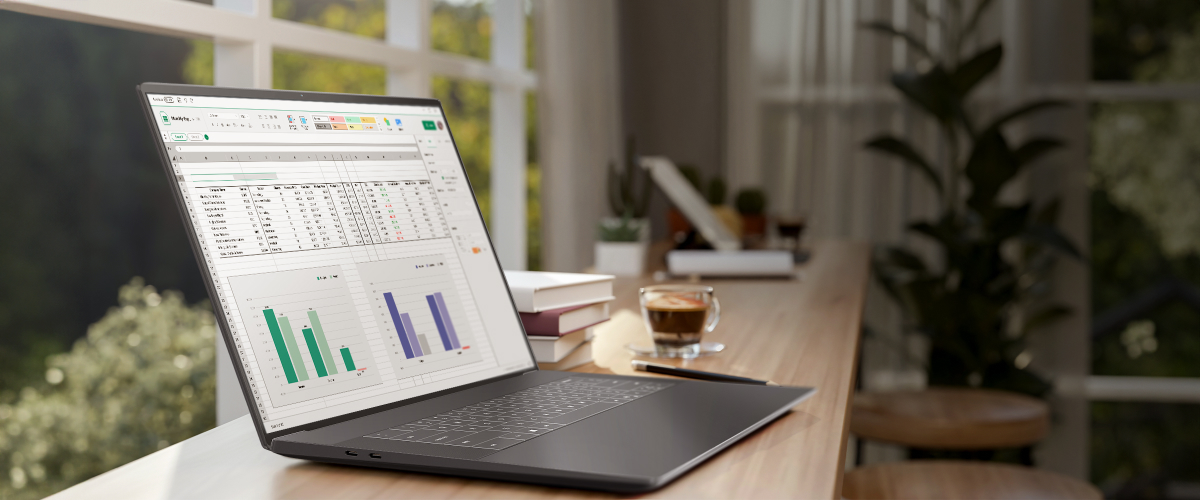 A spreadsheet is displayed on a laptop screen on a cafe table, with a view of nature outside the window. LG Display's Tandem ATO technology improves battery efficiency by up to 40 percent, emphasizing the long hours of use with low power consumption.