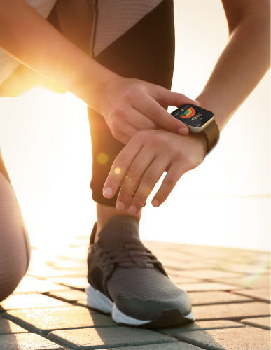 A person in sweatpants is operating a smartwatch on one's wrist, and the screen is clearly visible despite the sun shining strongly from the behind.