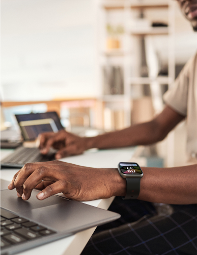 A person is working on a laptop in an office with a smartwatch strapped to his left wrist.