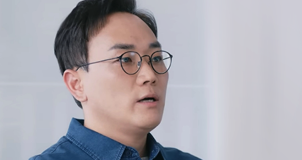 Team leader Park Jung-soo, wearing a blue shirt, is looking sideways and explaining OLED deuterium.